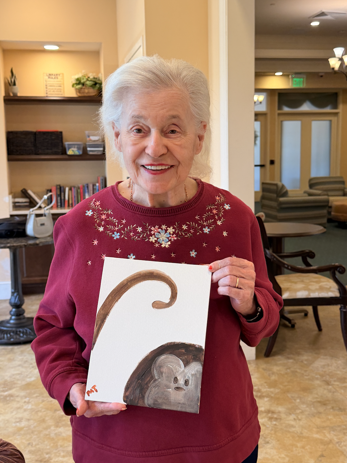 Resident smiling and holding up her finished animal-themed painting.