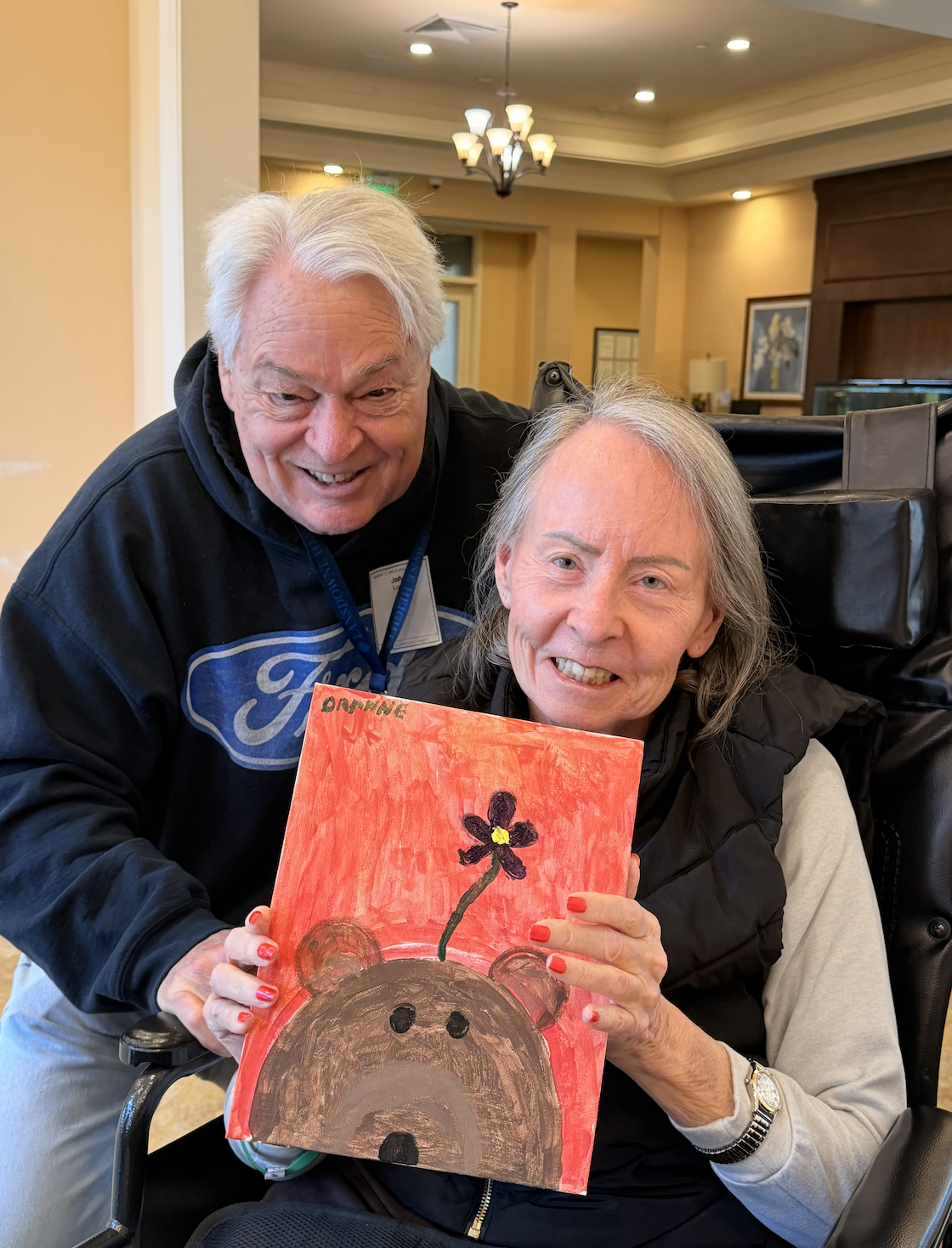 Two people smiling and holding a finished painting together.