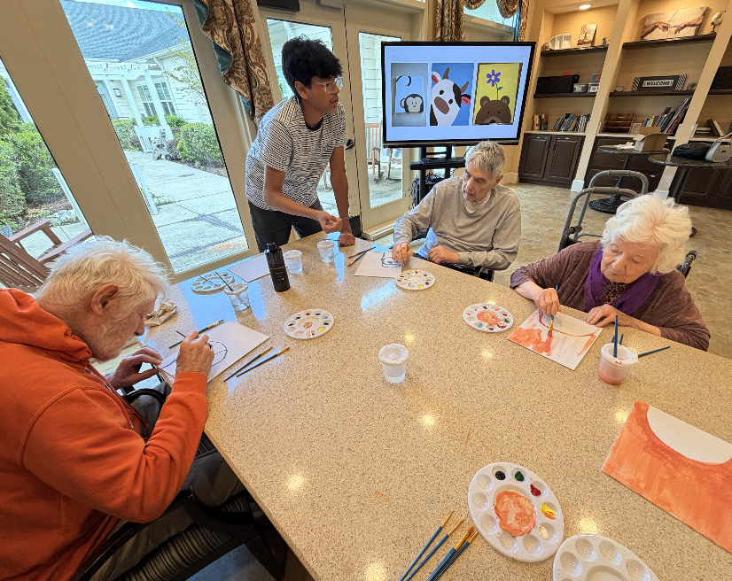 Student volunteer standing beside residents during a painting workshop.